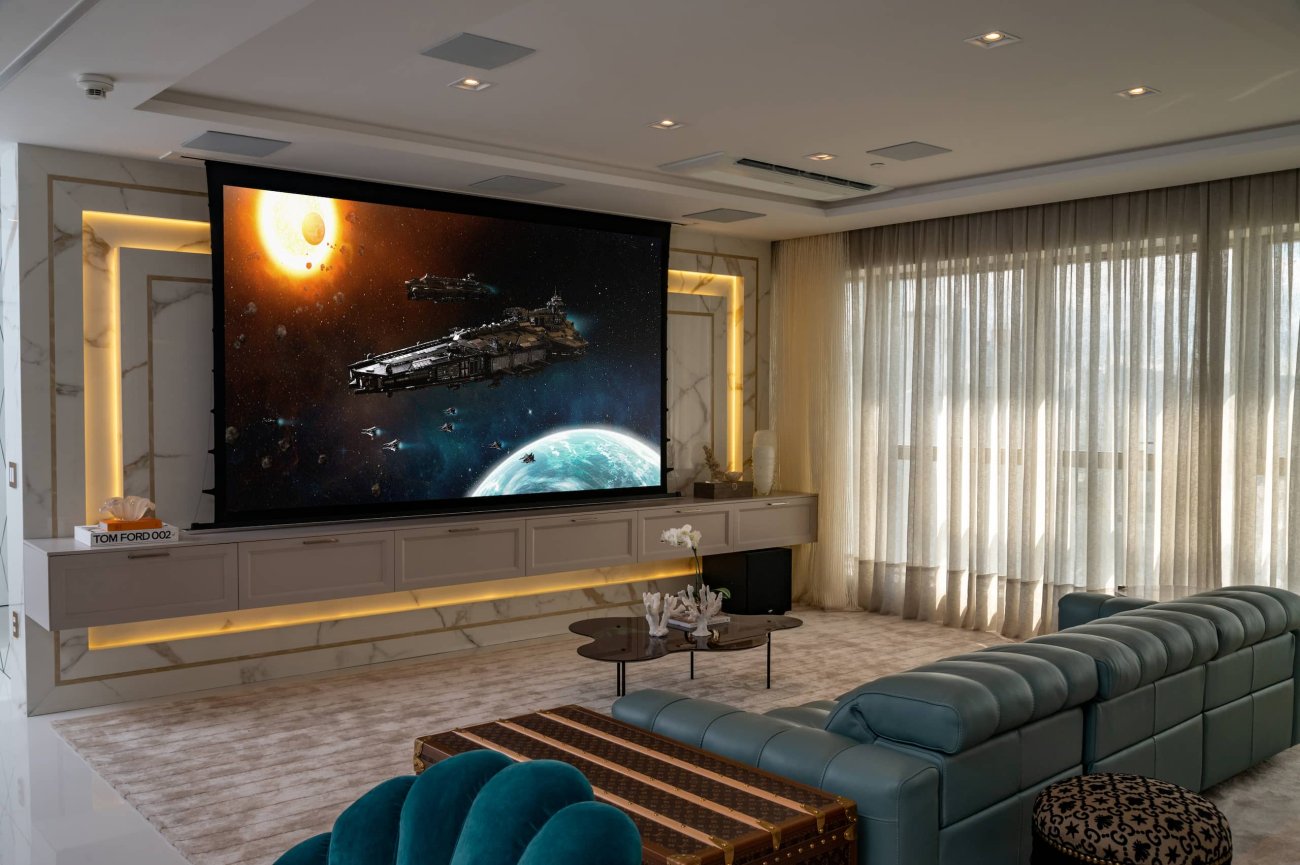 No living, principal ambiente do imóvel, foram instaladas soluções high-tech de áudio e vídeo para oferecer aos moradores, qualidade de cinema para assistirem seus filmes e produções preferidas. Este espaço conta com projetor 4K a laser, de alta qualidade e profundidade de imagem associado, a uma tela de projeção de 125", produzida em tecido tecnológico de alto contraste.