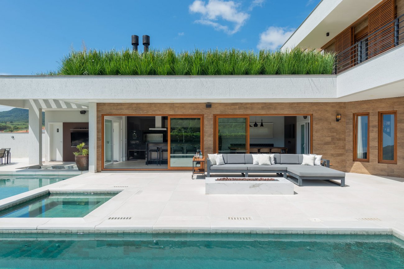 A piscina destaca-se por ser completamente revestida em pedra Hijau, uma pedra proveniente da Indonésia e de origem vulcânica. Seu entorno é todo revestido em piso cimentício atérmico, mantendo o conforto ao estar na área externa, até nos dias mais quentes. Ainda para os dias mais frios, foi projetada uma lareira de 1,80m de comprimento, posicionada estrategicamente para o uso no inverno, sendo que a piscina conta também com aquecimento.