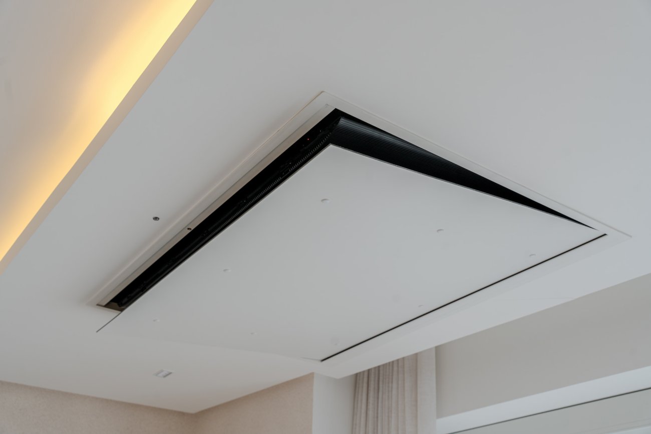 Na suíte master, o conforto se traduz em leveza. Um flap motorizado compatível com TV de 55 polegadas, integrado ao sistema de automação, permite que a tela fique totalmente embutida no teto e só apareça quando acionada. Assim, a tecnologia não invade o espaço: ela se esconde para que o silêncio e o descanso sejam protagonistas, revelando-se apenas quando o momento pede.